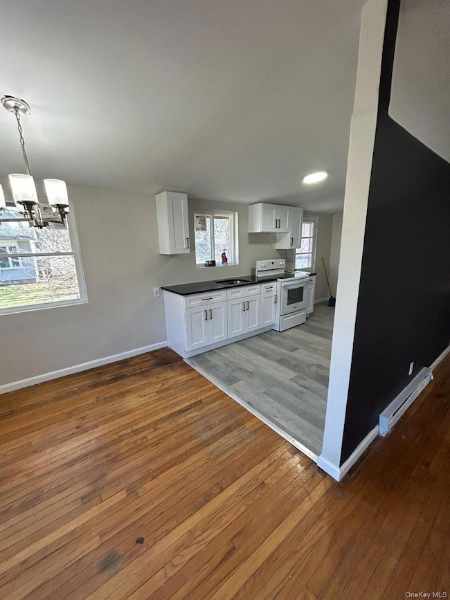 Kitchen featuring dark countertops, white cabinetry, light wood-style floors, a baseboard heating unit, and electric range
