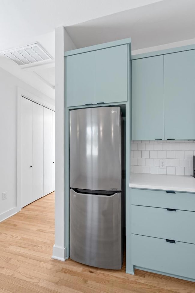 Kitchen featuring freestanding refrigerator, light wood finished floors, blue cabinetry, modern cabinets, and decorative backsplash