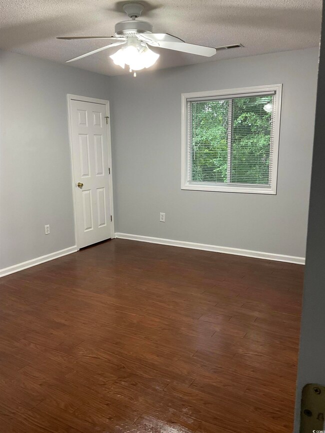Empty room featuring a ceiling fan, dark wood-type flooring, and a textured ceiling
