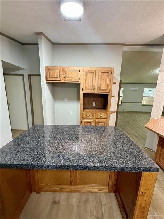 Kitchen with a textured ceiling, light wood-style floors, ornamental molding, and dark stone counters