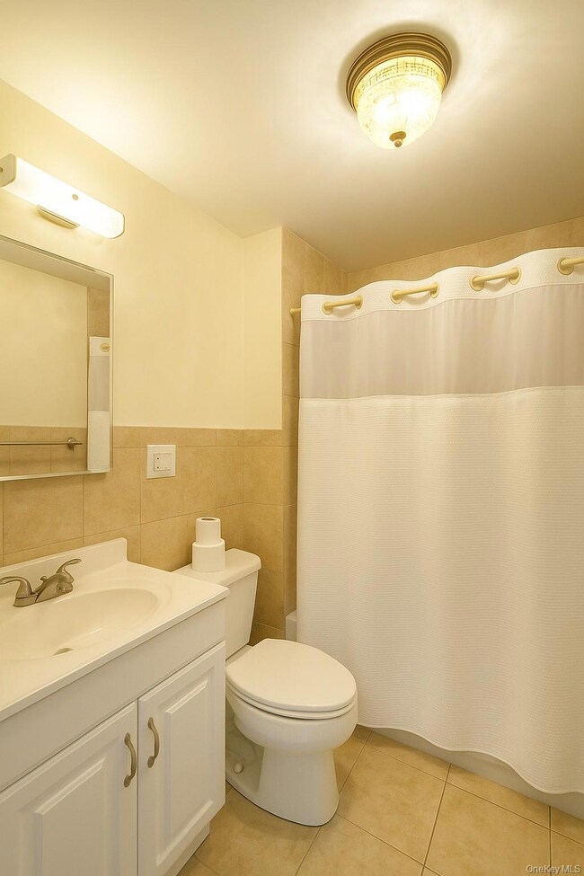Bathroom with vanity, curtained shower, tile walls, light tile patterned floors, and a wainscoted wall