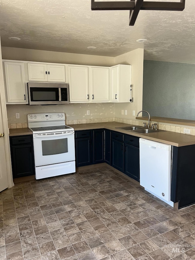 Kitchen with white appliances, white cabinets, a textured ceiling, and a peninsula
