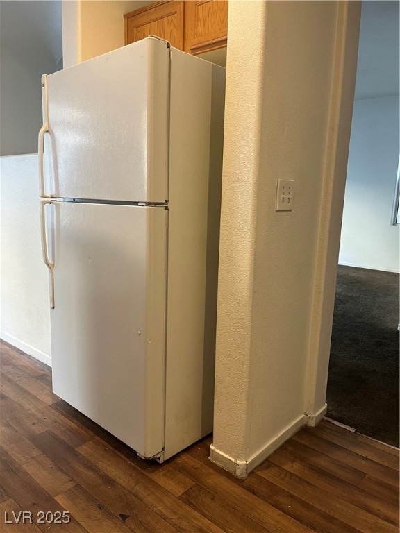 Kitchen with freestanding refrigerator, dark wood finished floors, and a textured wall