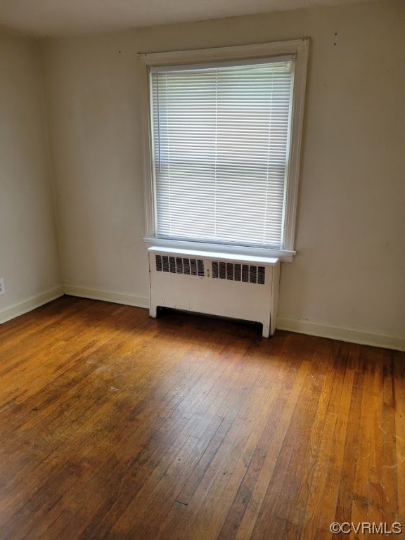 Spare room featuring plenty of natural light, dark hardwood / wood-style flooring, and radiator heating unit