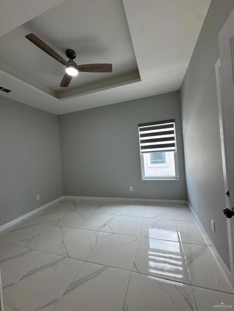 Unfurnished room featuring baseboards, light marble finish floors, a tray ceiling, and a ceiling fan