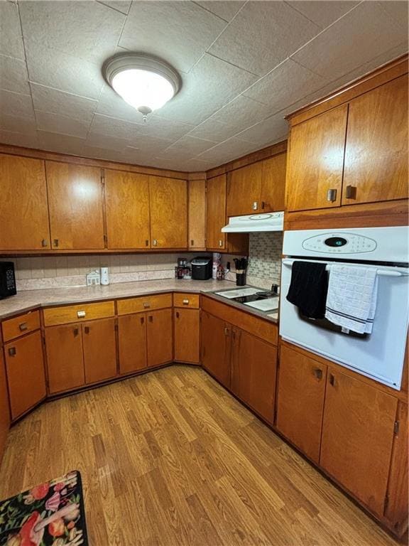 Kitchen with tasteful backsplash, ventilation hood, light wood-type flooring, oven, and stovetop
