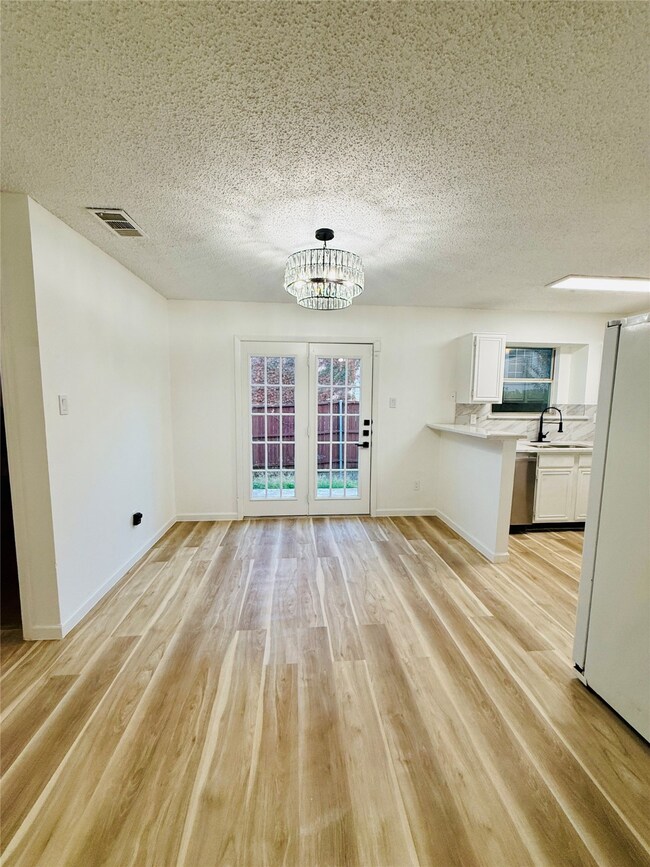 Unfurnished dining area with a textured ceiling, light wood-type flooring, and a chandelier