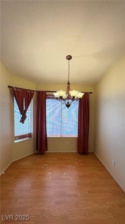 Unfurnished dining area featuring a chandelier, light wood-style floors, and a textured ceiling