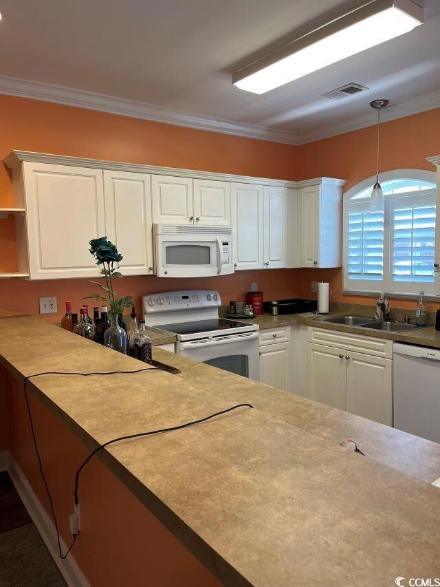 Kitchen featuring white appliances, white cabinets, a sink, ornamental molding, and decorative light fixtures
