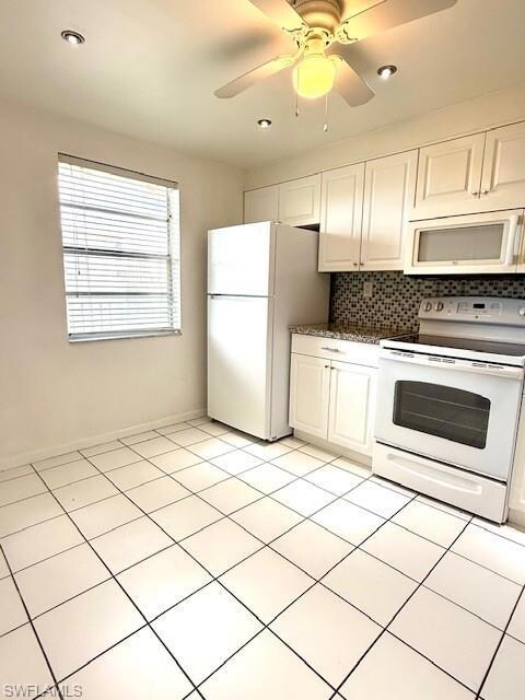 Kitchen featuring white appliances, tasteful backsplash, white cabinets, dark countertops, and ceiling fan
