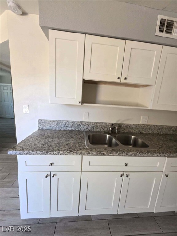 Kitchen with a sink, white cabinetry, dark stone c