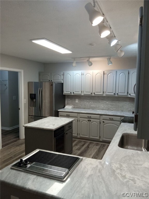 Kitchen with a center island, tasteful backsplash, beverage cooler, stainless steel fridge, and rail lighting