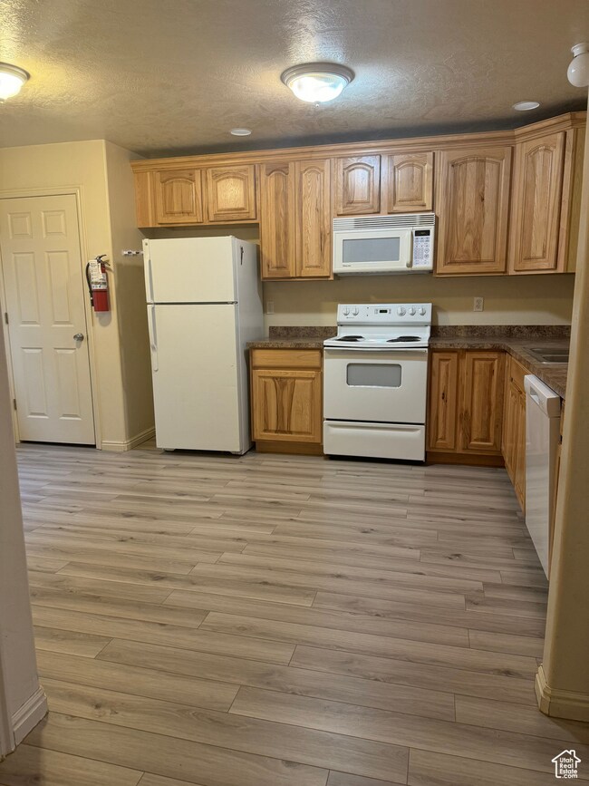 Kitchen featuring a textured ceiling, light hardwood / wood-style flooring, and white appliances