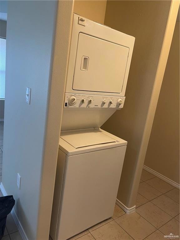 Washroom with stacked washing machine and dryer, light tile patterned floors, and baseboards