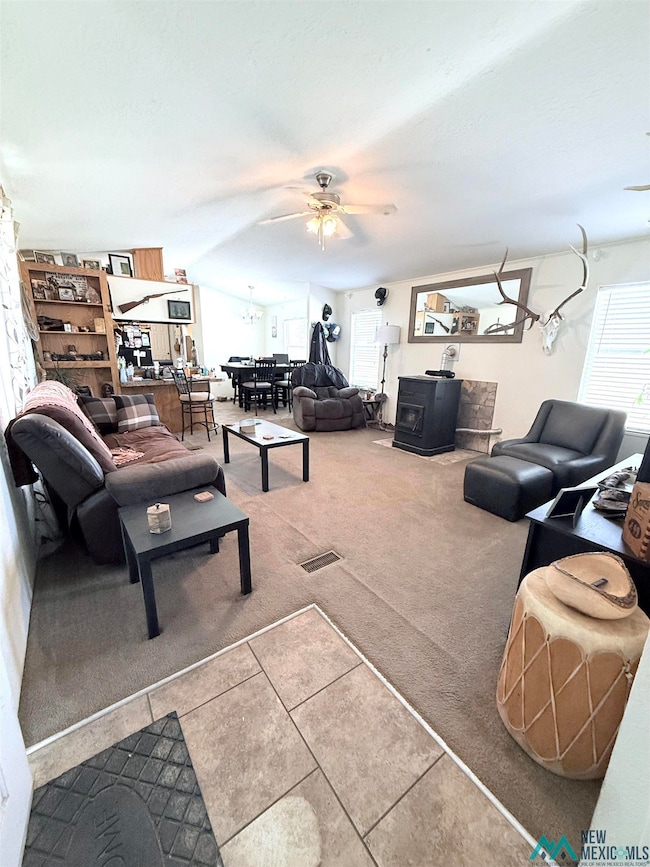 Living area featuring a wood stove, carpet, tile patterned flooring, and ceiling fan