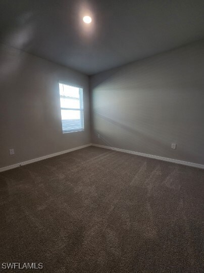 Empty room featuring baseboards and dark carpet
