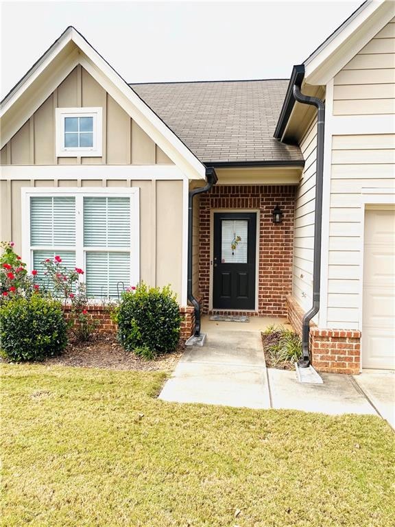 Doorway to property with brick siding, board and batten siding, a yard, a shingled roof, and a garage