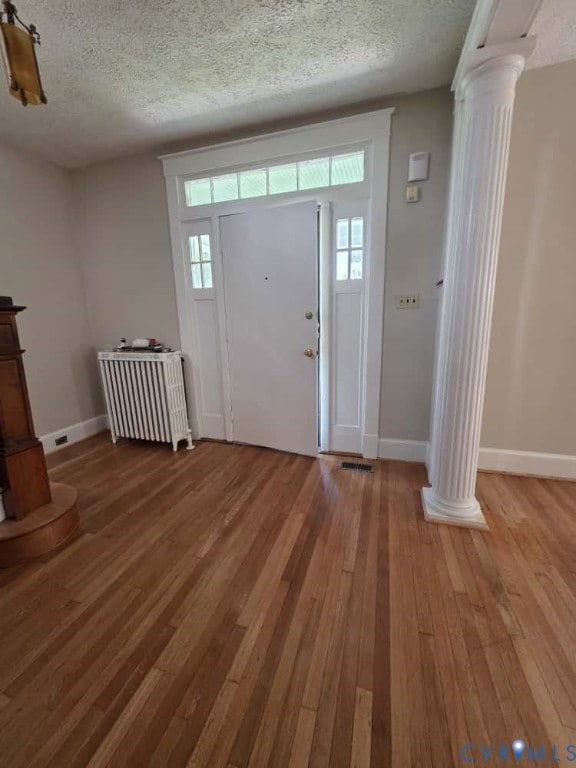 Foyer featuring ornate columns, a textured ceiling, radiator, light wood-style floors, and healthy amount of natural light
