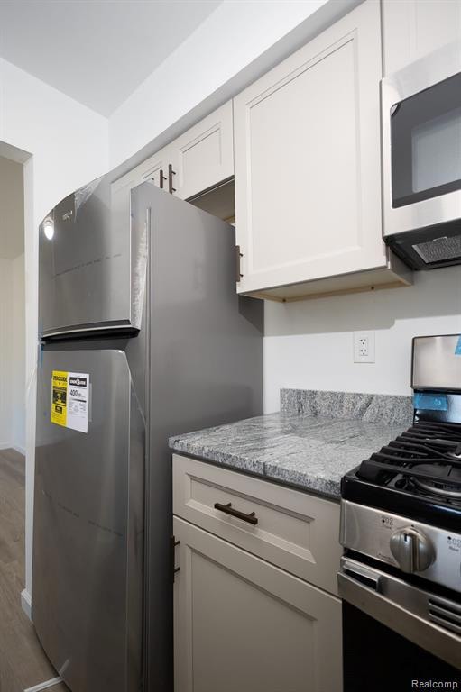 Kitchen featuring appliances with stainless steel finishes, white cabinets, light stone counters, and wood finished floors