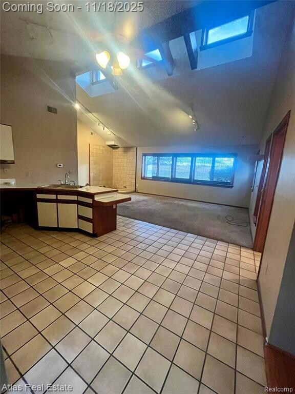 Kitchen with light tile patterned flooring, a peninsula, white cabinets, high vaulted ceiling, and light colored carpet