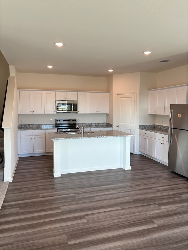 Kitchen with white cabinetry, fridge, recessed lighting, stove, and dark stone counters
