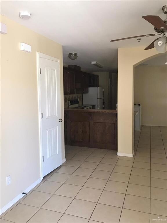 Kitchen with dark brown cabinets, white appliances, ceiling fan, and light tile patterned flooring