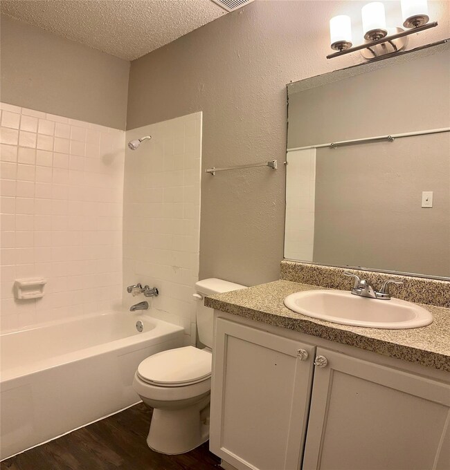 Full bath with a textured ceiling, shower / tub combination, dark wood-type flooring, vanity, and a textured wall