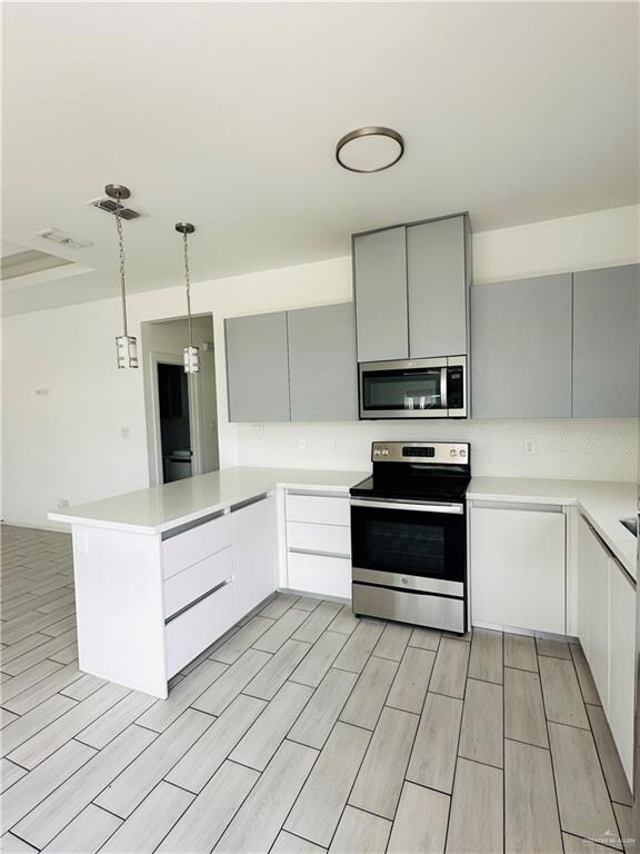 Kitchen with stainless steel appliances, a peninsula, gray cabinetry, and light countertops