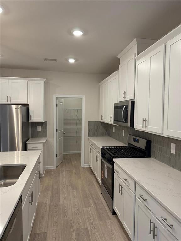 Kitchen with appliances with stainless steel finishes, white cabinets, decorative backsplash, light wood-style floors, and light stone counters