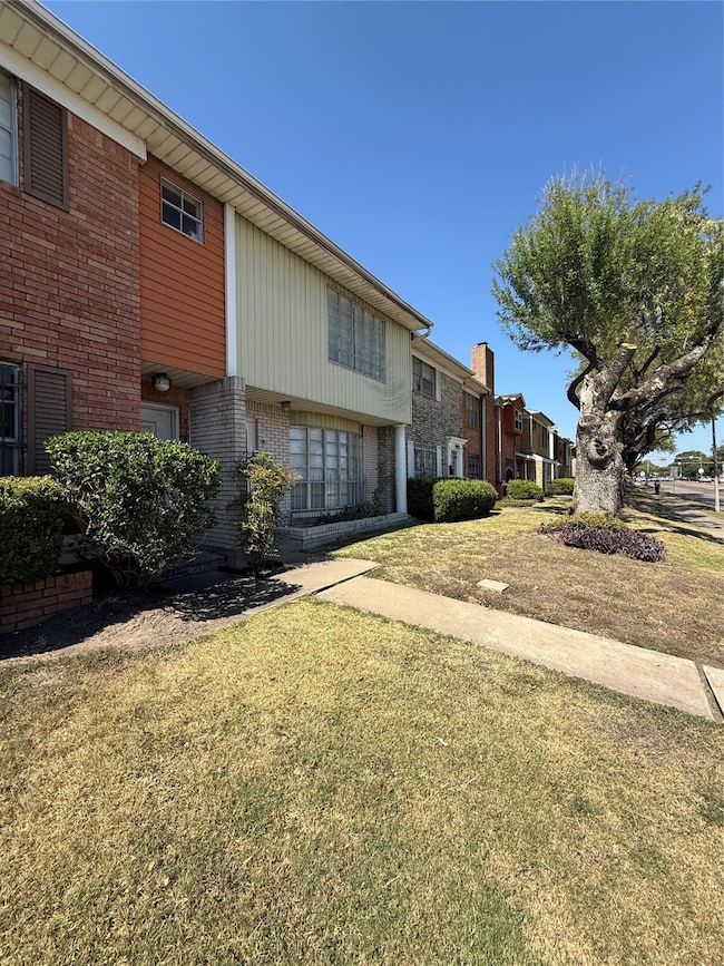 brick and siding exterior, featuring a well-maintained front lawn and mature trees. It has large front windows and is located in a row of similar homes, offering a charming suburban feel.