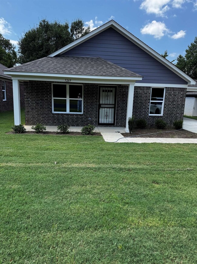 Ranch-style home featuring a front lawn, a shingled roof, brick siding, and a porch