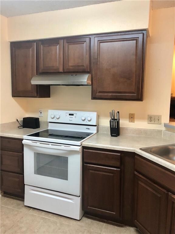 Kitchen with electric range, dark brown cabinets, and under cabinet range hood