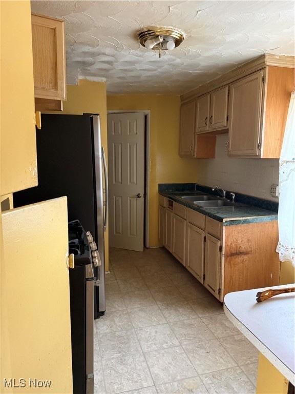Kitchen featuring decorative backsplash, dark countertops, a textured ceiling, light brown cabinetry, and refrigerator