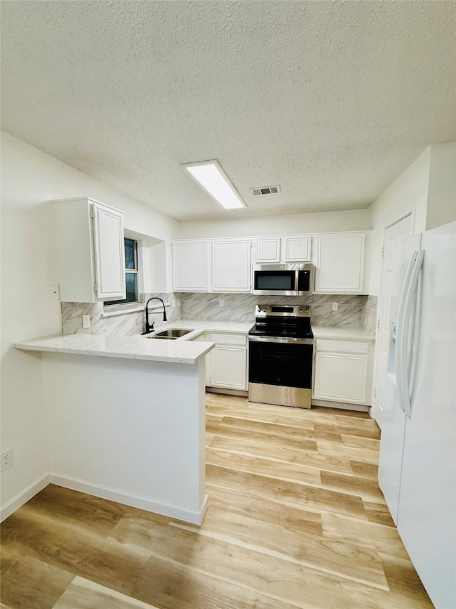 Kitchen featuring decorative backsplash, stainless steel appliances, white cabinets, a peninsula, and a textured ceiling
