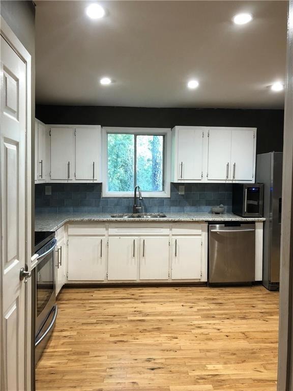 Kitchen with appliances with stainless steel finishes, white cabinetry, decorative backsplash, light wood finished floors, and recessed lighting