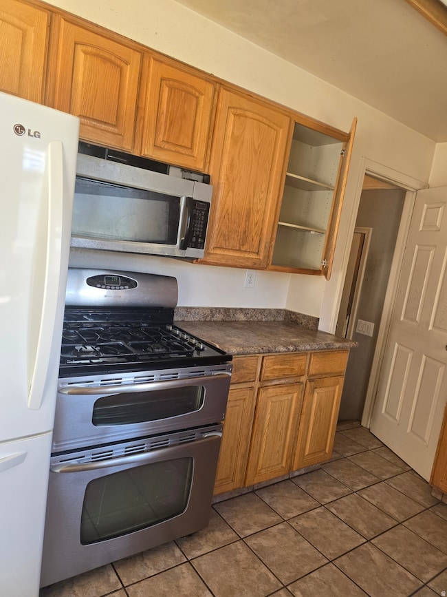 Kitchen featuring appliances with stainless steel finishes, brown cabinets, dark countertops, dark tile patterned flooring, and open shelves