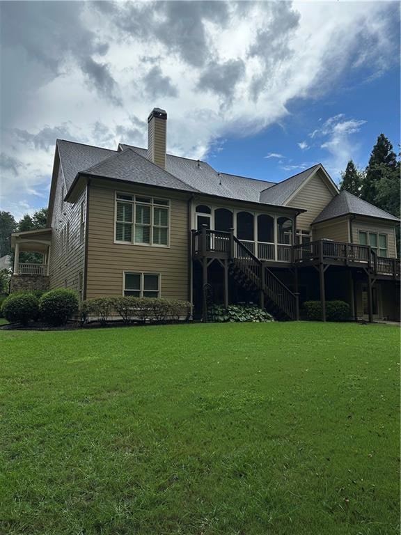 Back of property featuring a wooden deck, a chimney, and a yard
