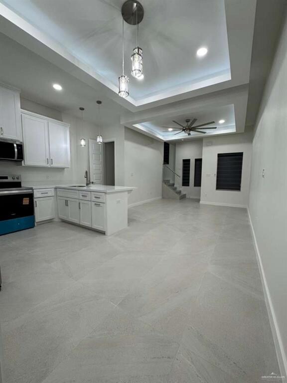 Kitchen featuring a raised ceiling, white cabinetry, appliances with stainless steel finishes, pendant lighting, and a peninsula
