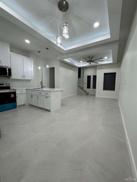 Kitchen featuring a raised ceiling, white cabinetry, appliances with stainless steel finishes, pendant lighting, and a peninsula
