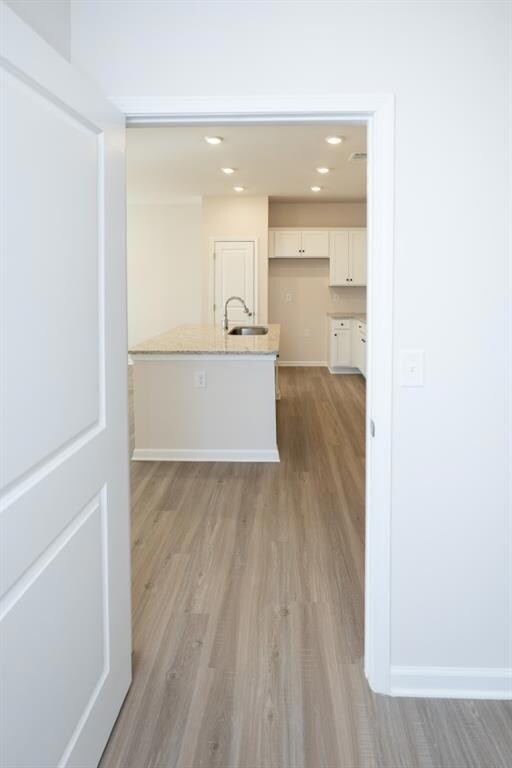Kitchen featuring light wood finished floors, a sink, white cabinets, light stone countertops, and a center island with sink