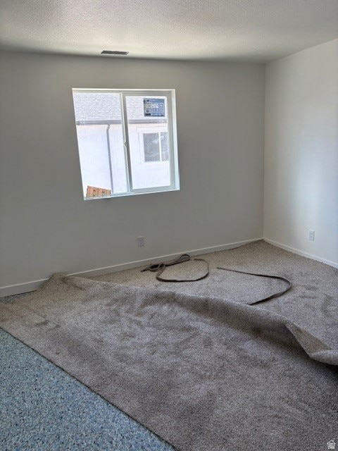 Carpeted empty room featuring a textured ceiling and baseboards