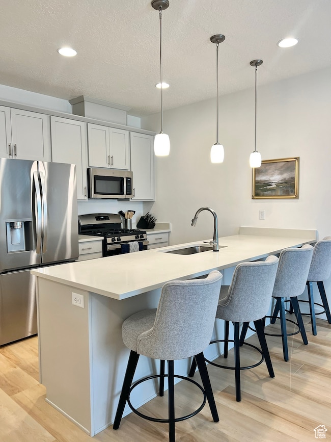 Kitchen featuring stainless steel appliances, a breakfast bar area, a peninsula, light wood-style flooring, and pendant lighting