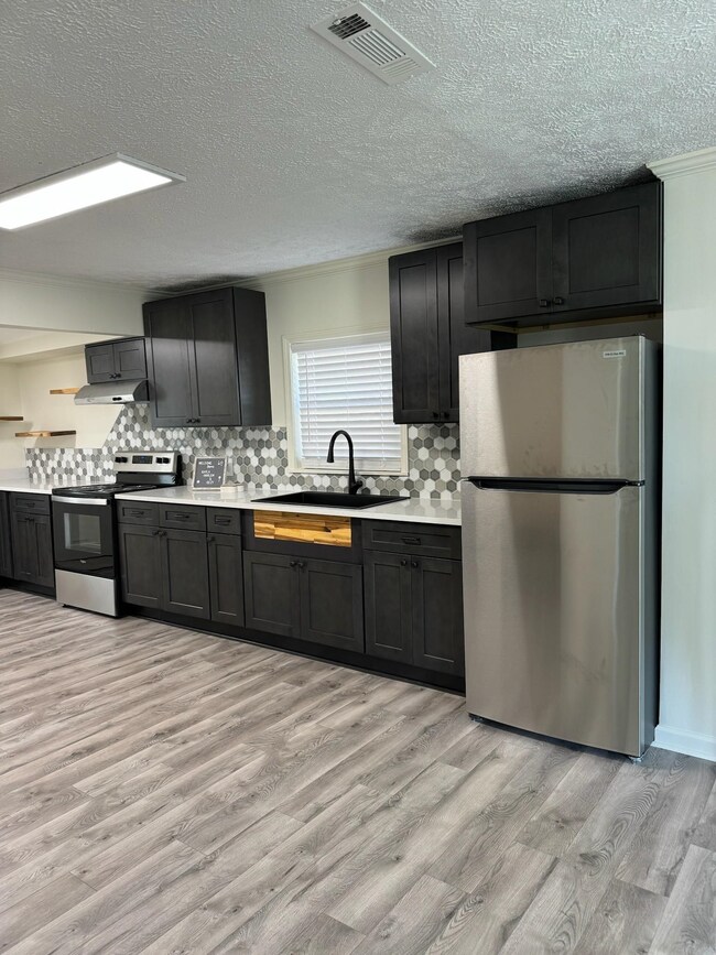 Kitchen with stainless steel appliances, a sink, light wood-type flooring, light countertops, and decorative backsplash