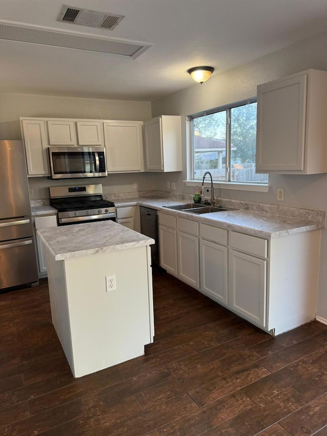 Kitchen with white cabinets, light countertops, appliances with stainless steel finishes, a center island, and dark wood-style floors