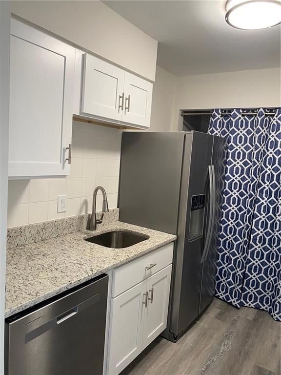 Kitchen with dishwasher, light wood-type flooring, white cabinets, light stone counters, and tasteful backsplash