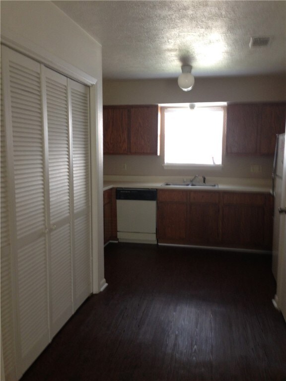 Kitchen featuring visible vents, light countertops, dark wood-style flooring, dishwasher, and brown cabinetry