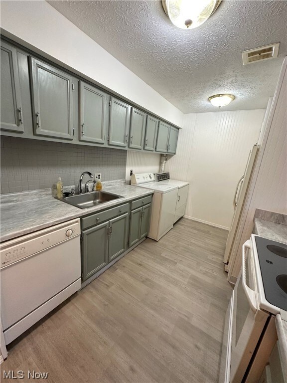 Kitchen with washer and clothes dryer, sink, light wood-type flooring, and white dishwasher