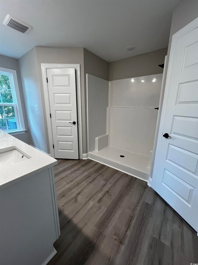 Bathroom featuring double vanity, a shower stall, and dark wood-style flooring