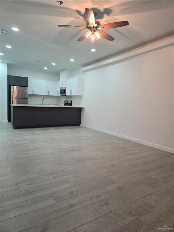 Kitchen featuring sink, kitchen peninsula, refrigerator, white cabinets, and light wood-type flooring
