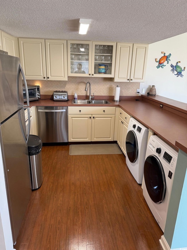 Kitchen with dark wood-style flooring, cream cabinets, independent washer and dryer, appliances with stainless steel finishes, and a sink